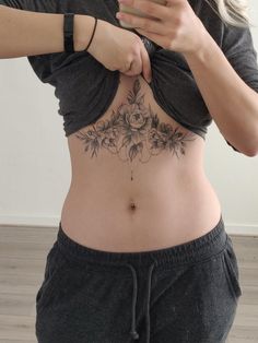 a woman with a flower tattoo on her stomach taking a selfie in the mirror