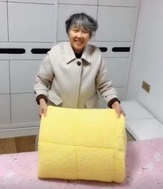 an older woman is holding up a yellow blanket