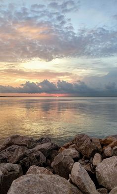 the sun is setting over the ocean with rocks on the shore and clouds in the sky