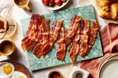 bacon strips are laid out on a cutting board next to bowls of fruit and coffee