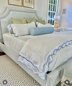 a white bed with blue trim and pillows in a bedroom next to a window,