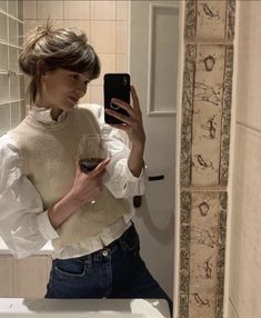 a woman taking a selfie in the bathroom with a glass of wine on her phone