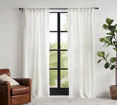 a living room with white curtains and a brown leather chair in front of the window