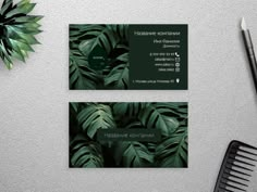 two business cards with green leaves on them next to a hair comb and scissors,