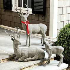 three deer statues sitting on the steps in front of a house with a red ribbon tied around their necks