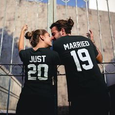 a man and woman in matching shirts standing next to each other near a metal fence