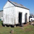 an old white building sitting in the middle of a grassy field next to a fire hydrant