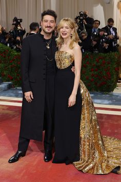 a man and woman standing next to each other on a red carpet with cameras in the background