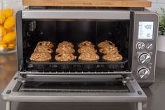 three cookies are being cooked in an open silver toaster oven on a countertop