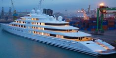 a large white boat is docked in the water at dusk with other boats and cranes around it