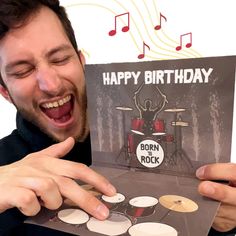 a man holding up a happy birthday card with drums and music notes in front of him