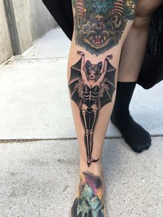 a woman's leg with a tattoo on it that has a bat and demon on it