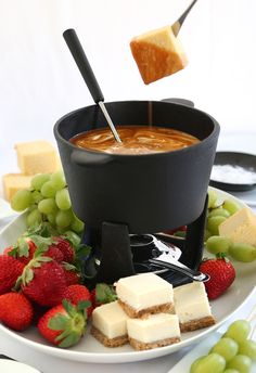 a plate with cheese, crackers and strawberries on it next to a fonding pot