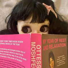 a doll with long black hair is holding a book in front of her face and looking at the camera