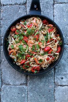 a skillet filled with pasta and shrimp on top of a stone floor next to a brick sidewalk