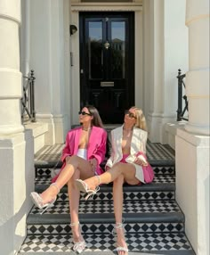 two women sitting on steps in front of a door with their legs crossed and one wearing heels