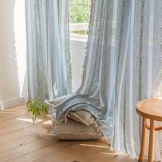 a room with wooden floors and curtains on the windowsill, there is a small round table in front of the window