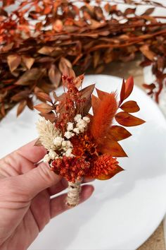 a person holding a bouquet of flowers on a white plate with red and orange leaves