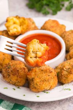 a white plate topped with fried food next to a bowl of tomato sauce and a fork