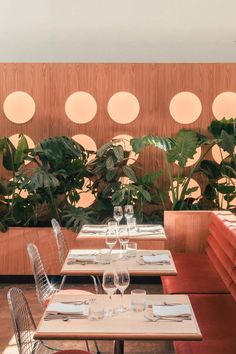 an empty restaurant table with place settings and plants on the wall behind it, along with red velvet seats