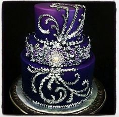 a three tiered purple cake with white and silver designs on it's sides