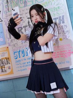 a woman in a skirt holding up a cell phone while standing next to a wall