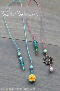 three necklaces with beads and charms hanging from them on a wooden surface, one has an orange flower