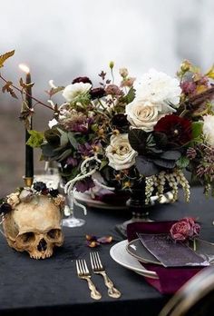 a table topped with a skull and flowers next to a wine glass filled with candles