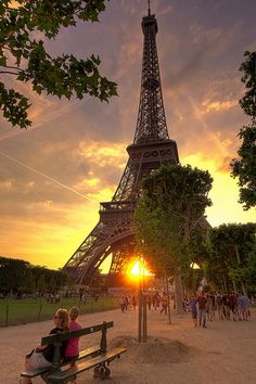 two people sitting on a bench in front of the eiffel tower at sunset