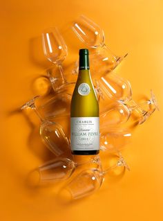 a bottle of wine sitting in front of many glasses on an orange background with the reflection of them