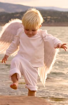 a little boy dressed up like an angel running on the beach with his wings spread