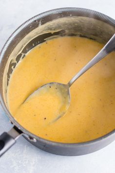 a ladle filled with yellow liquid sitting on top of a white counter next to a black spoon