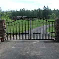 an iron gate with brick pillars leading to a driveway and grassy area in the background