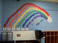 a rainbow painted on the side of a wall in a school room with lots of trash cans