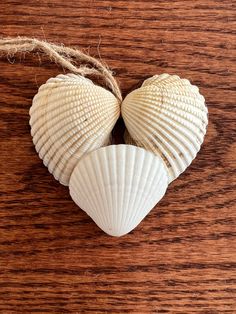 three seashells are arranged in the shape of a heart on a wooden surface