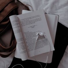 an open book with headphones on top of it next to a purse and earbuds