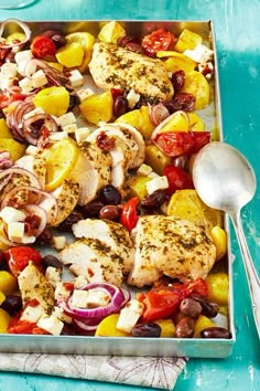 a pan filled with chicken, olives, peppers and onions next to a spoon