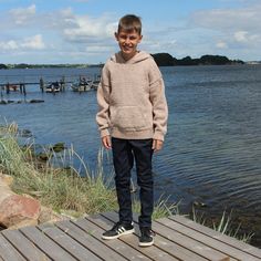 a young boy standing on a wooden dock next to the water with his hands in his pockets