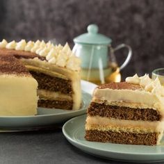 two plates with slices of cake on them next to a teapot and glass cup