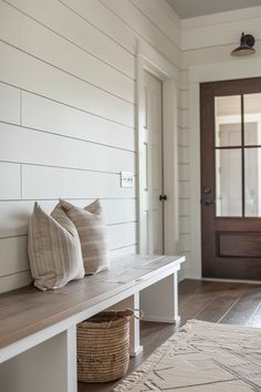 a bench with two pillows on it in front of a door and a basket next to it