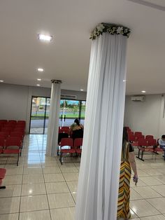 a woman is standing in the middle of a room with red chairs and white drapes