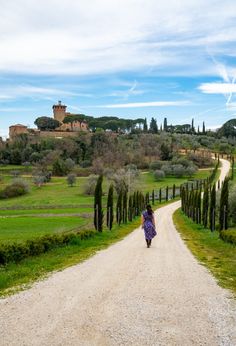 a woman walking down a dirt road in front of an old castle on top of a hill