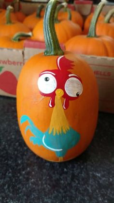 an orange pumpkin with a chicken painted on it's face and eyes, sitting in front of other pumpkins