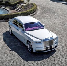 a white rolls royce parked in front of a fountain on a cobblestone driveway