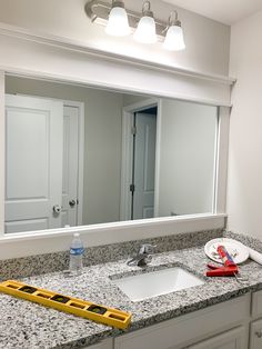 a bathroom sink under a large mirror next to a yellow tool