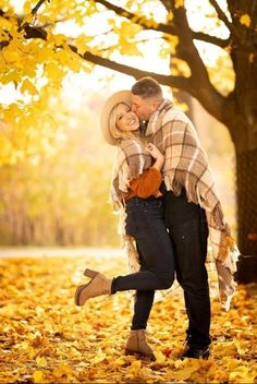 a man and woman hugging under a tree in the fall