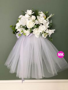 a bouquet of white flowers in a tulle skirt hanging on the wall with a pink sticker next to it