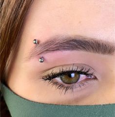 a woman's eye with piercings on her forehead and eyebrows, looking at the camera