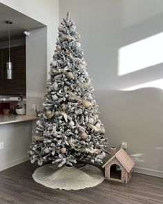 a white christmas tree in a living room next to a dog house and kitchen area