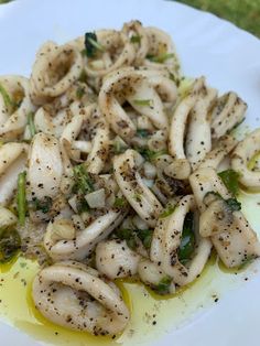 a white plate topped with squid and broccoli covered in olive oil on top of a green tablecloth